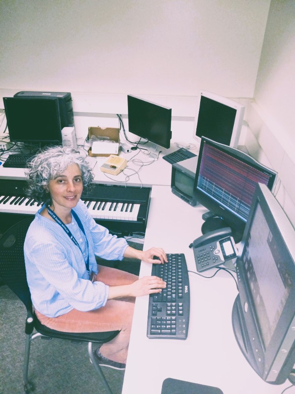 Isabelle Buard sits in front of two computer monitors with brain imaging data on them. To her left, is a piano keyboard.