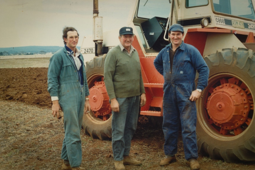 A scanned photograph shows three men in work suits standing outside next to a red tractor