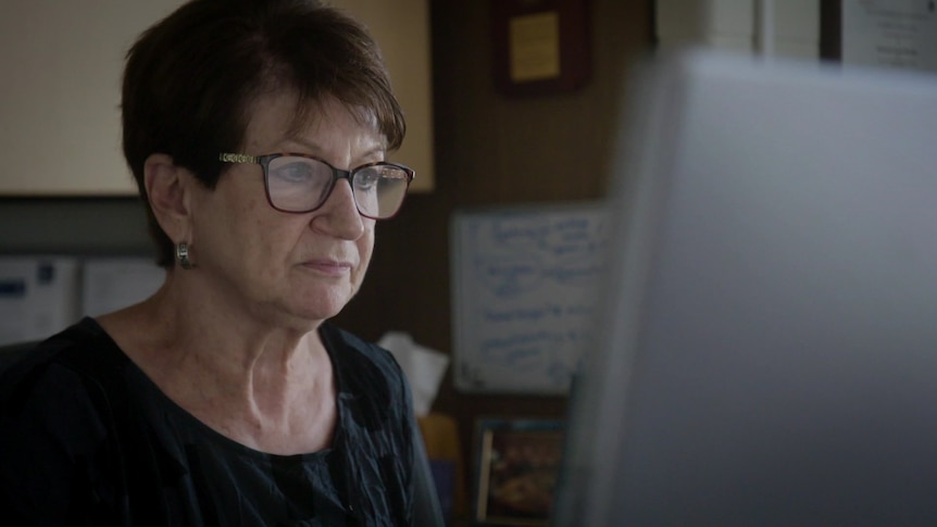 A middle-aged woman with short haircut wearing sits looking at a computer screen