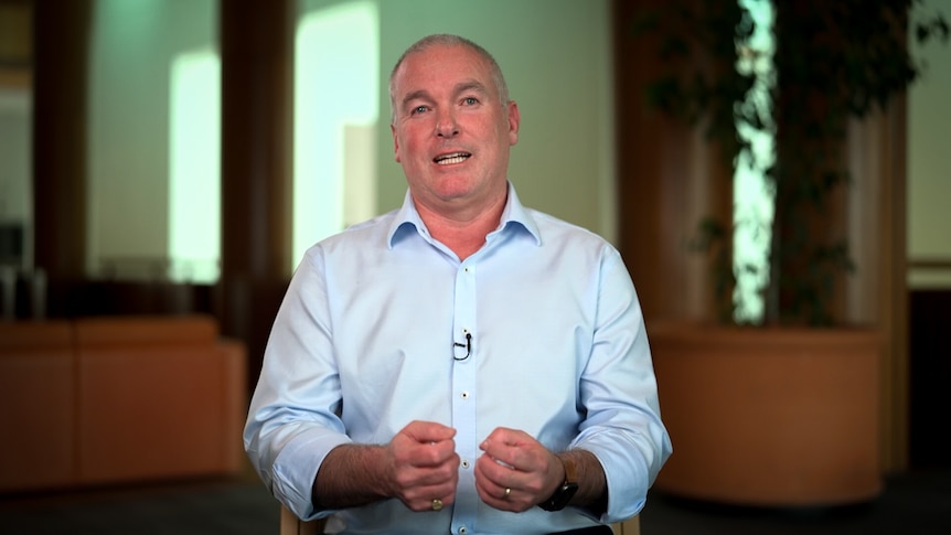 A man wearing a pale blue business shirt holds his hands in front of him