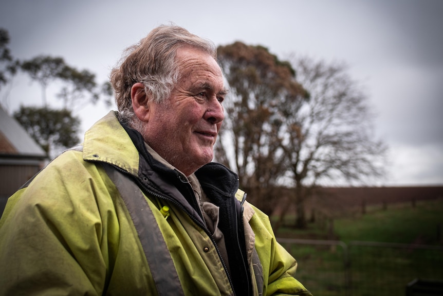 An older man wearing hi-vis coat smiles, photographed from the side, against a grey sky