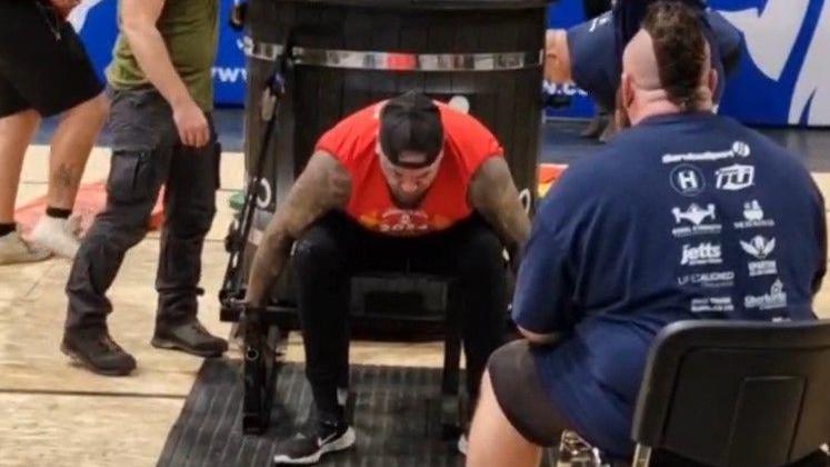 Shaun Slicker in a strongman competition. He is sitting and holding the handles of a trailer that is behind him, about to lift it.