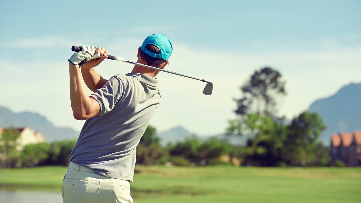 Golfer hitting golf shot with club on course while on summer vacation