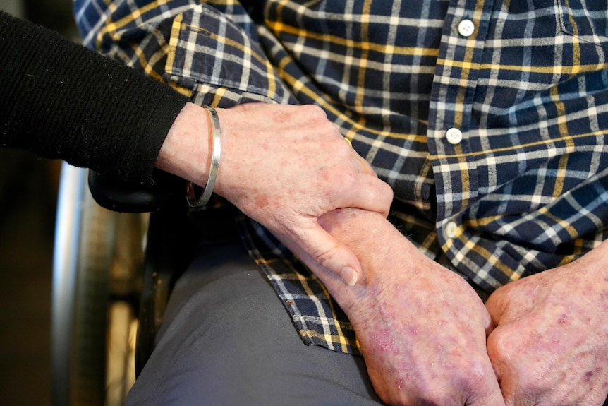 A closeup of Marcia's hand on John's, which is in his lap.
