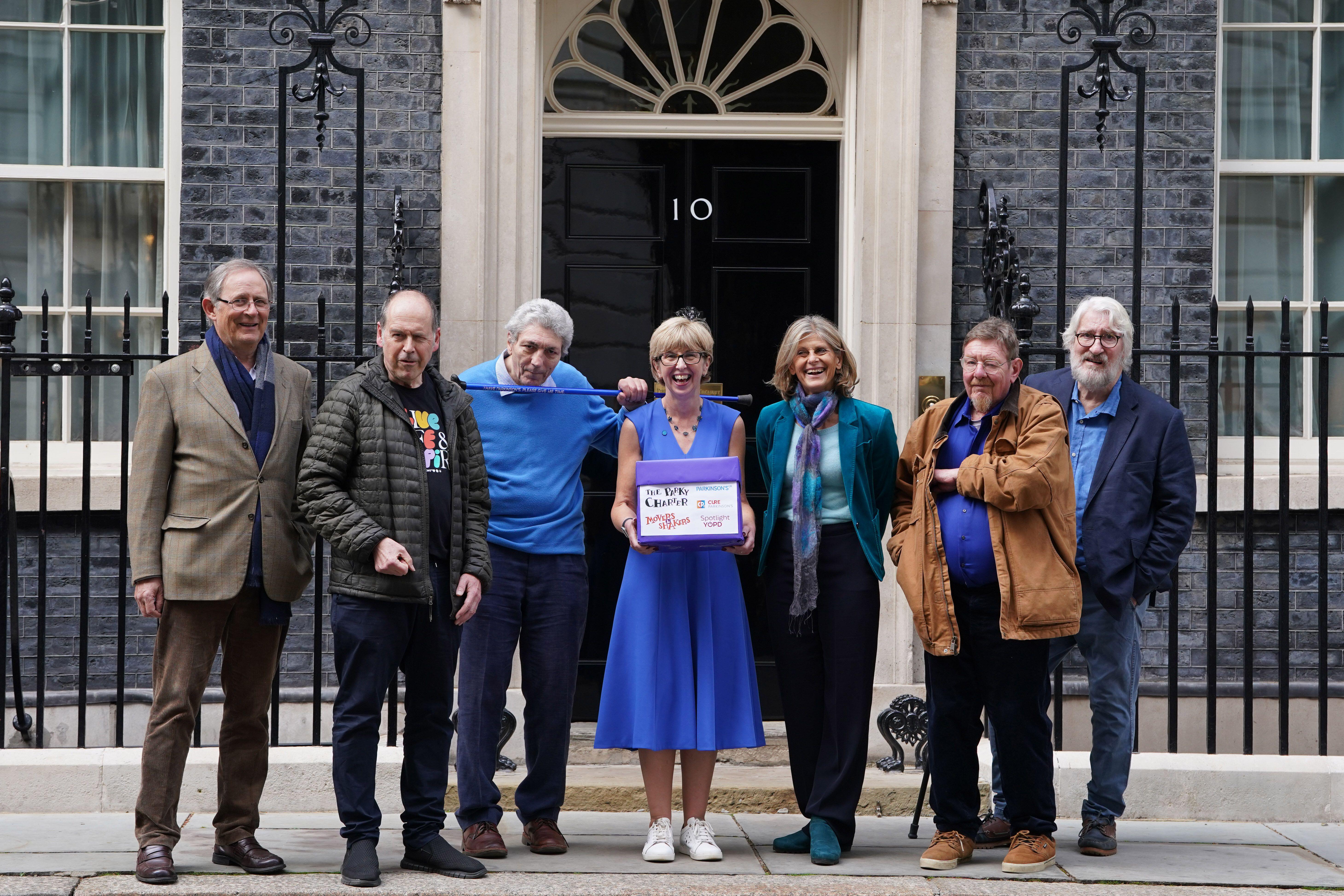 Seven people, including the hosts of The Movers and Shakers podcast and Parkinson's UK CEO Caroline Rassell, stand in front of 10 Downing Street, holding a "Parky Charter" petition.