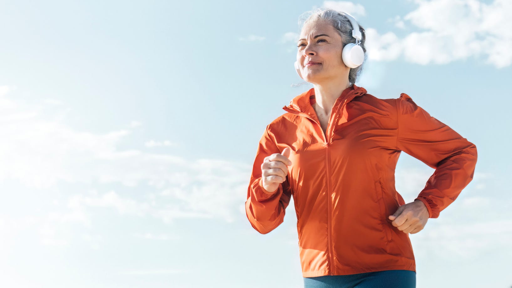 woman jogging outdoors wearing headphones and an orange jacket